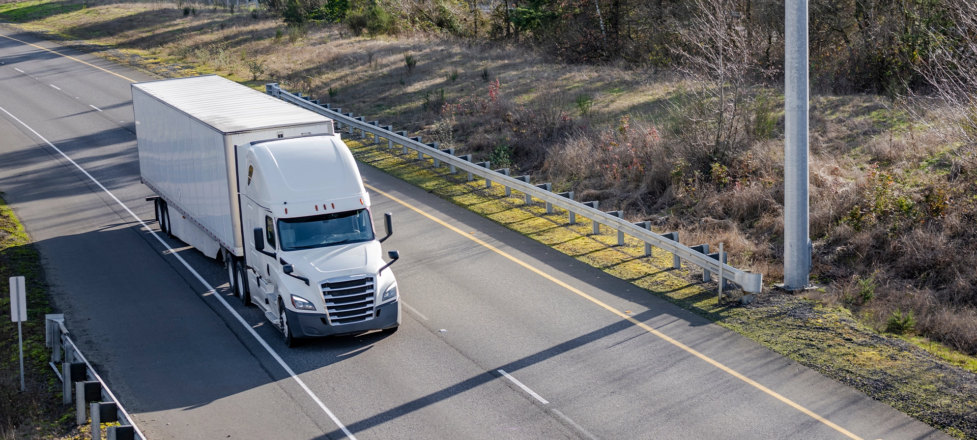 Classic big rig white semi truck tractor with sleeping compartment transporting commercial cargo in dry van semi trailer moving on the highway road intersection with one way traffic direction